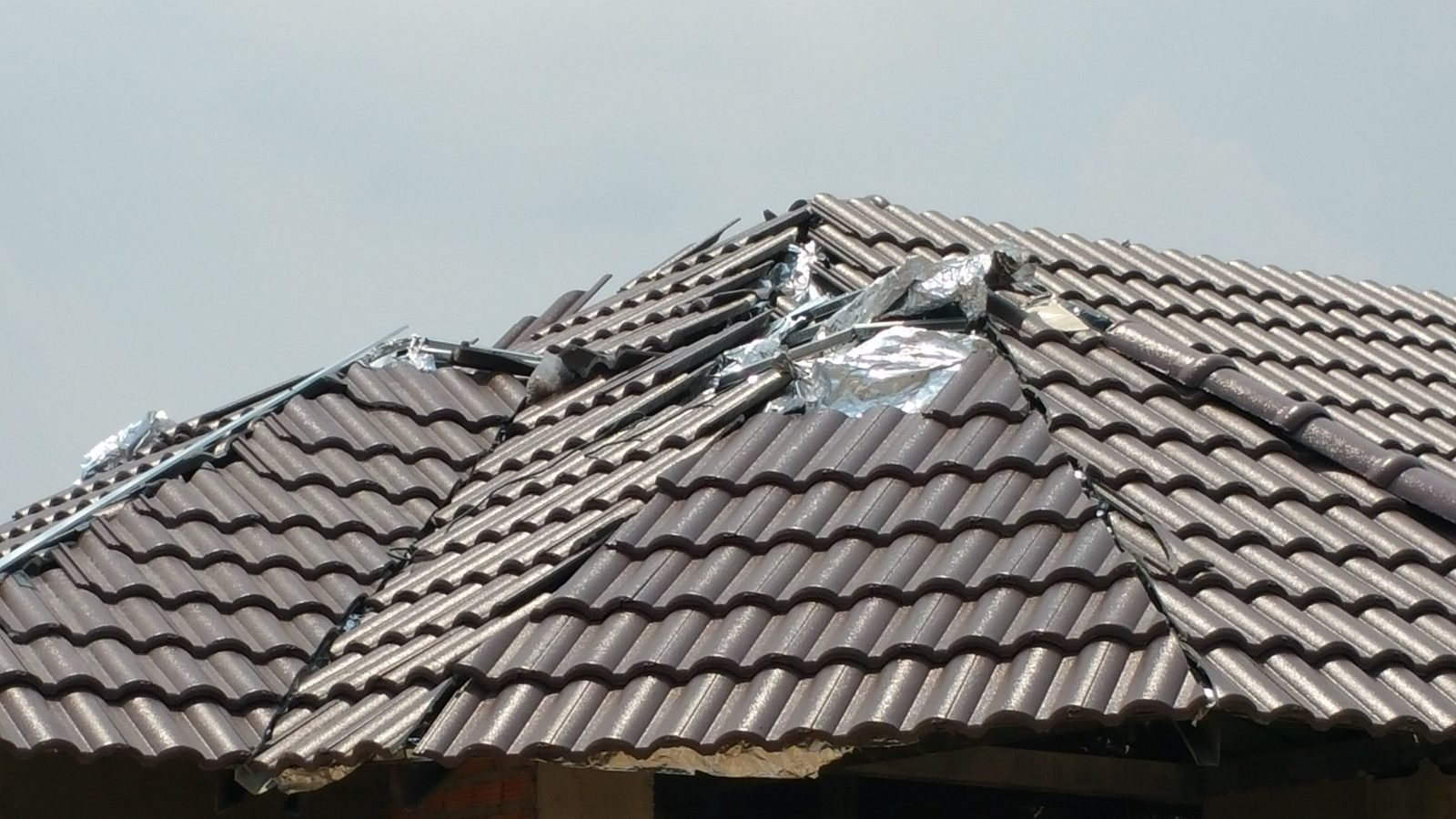 Damaged tile roof with broken and missing tiles and silver repair patching