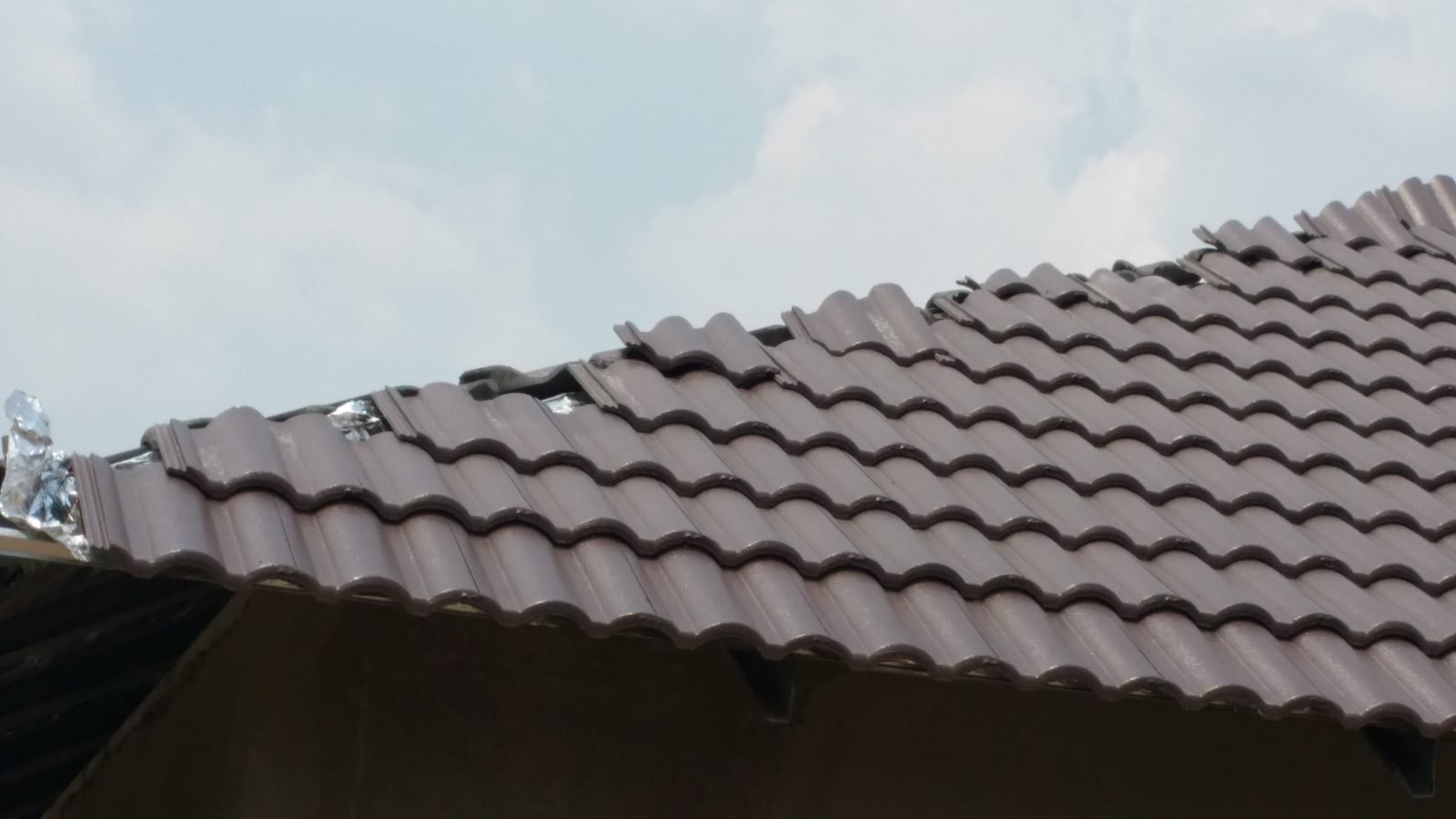 Tile roof repair in progress near the ridge, with lifted tiles and repair material visible